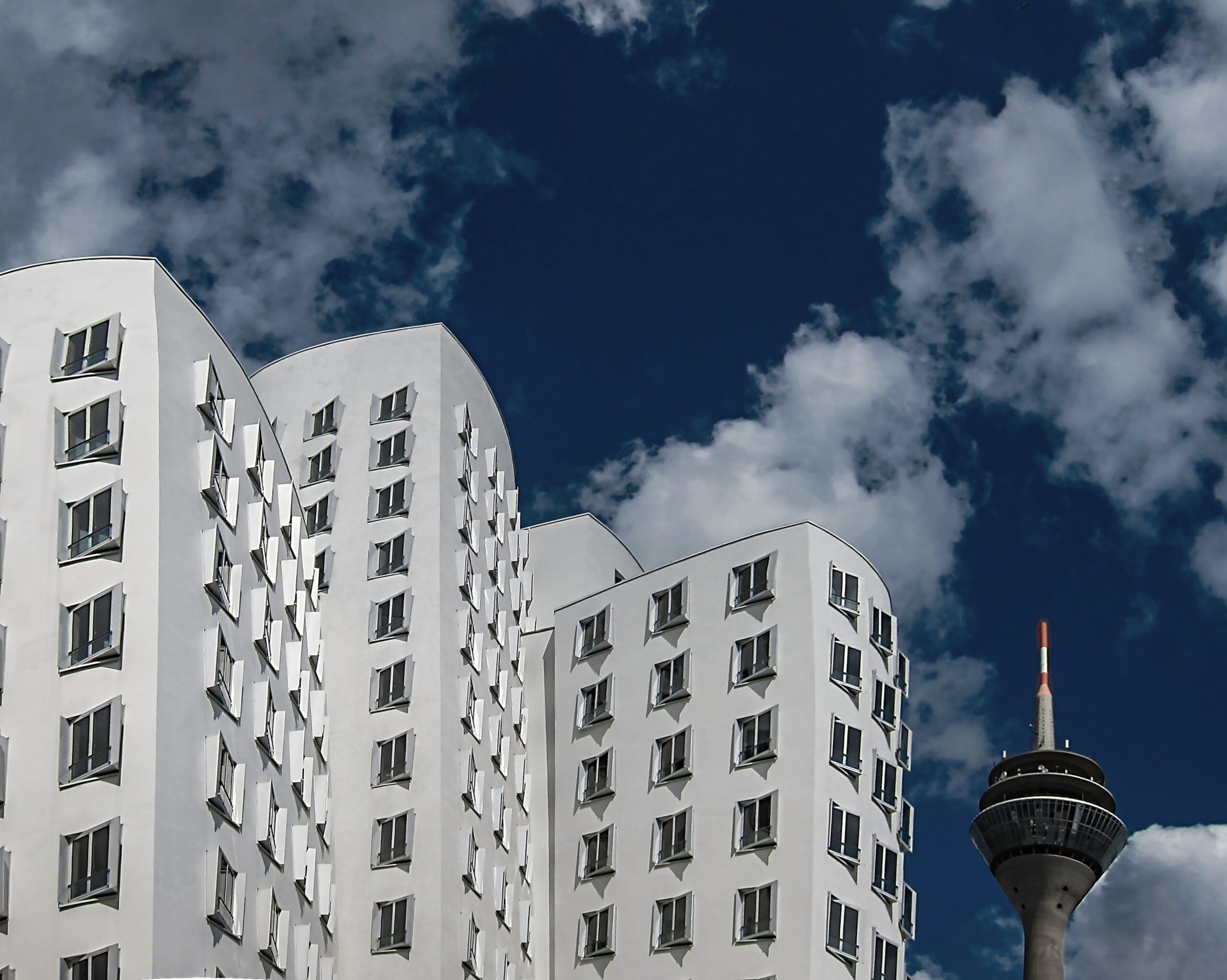 The white Gehry building in the Medienhafen from below, the Rheinturm on the right against clouds