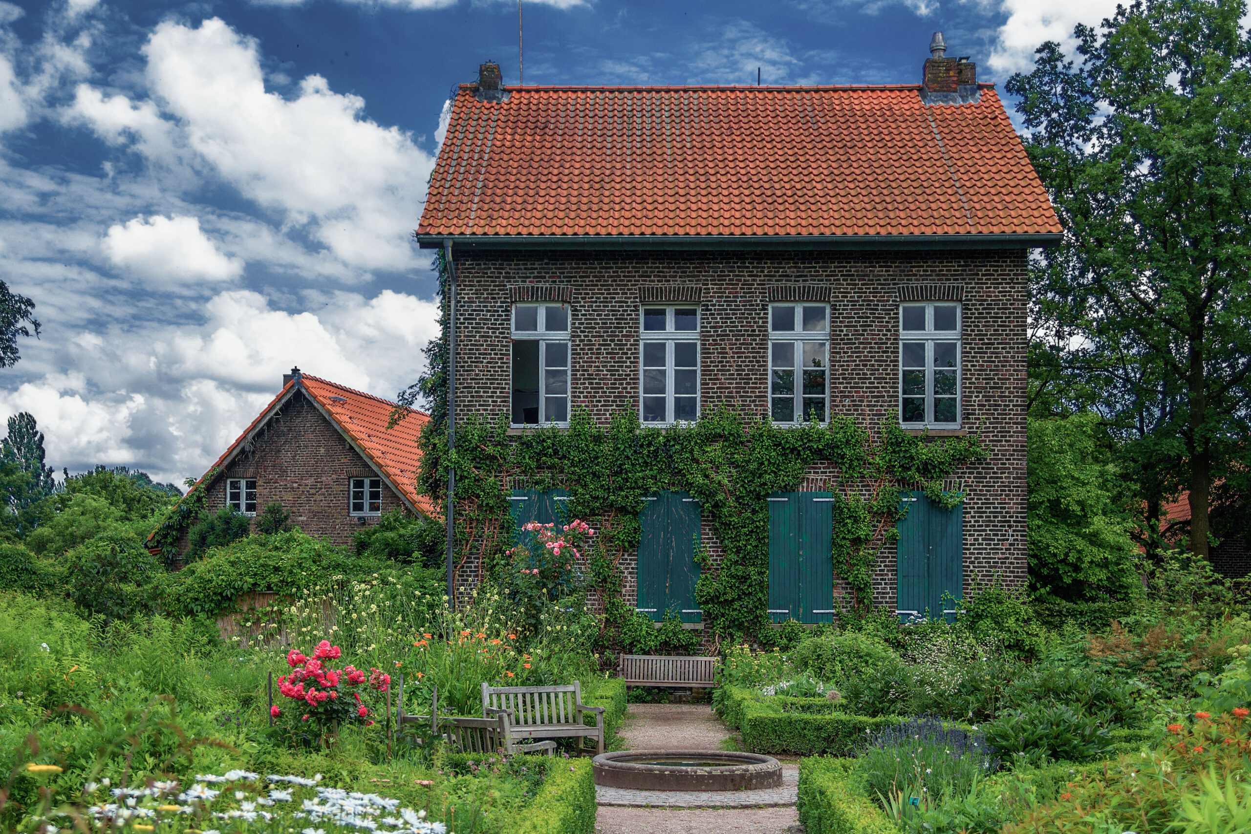 The Höfchen in Südpark, a brick house with green shutters and ivy, a flowering cottage garden in front